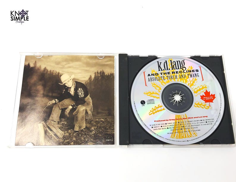 May include: A K.D. Lang and the Reclines "Absolute Torch and Twang" CD in a black jewel case. The CD has a silver surface with the album title and a Canadian maple leaf. The album art features a sepia-toned image of a person in a cowboy hat.
