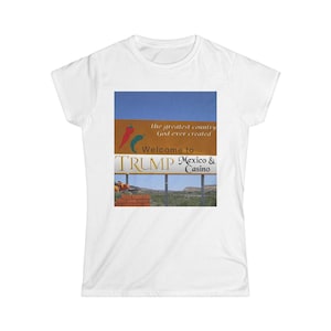 May include: White t-shirt featuring a graphic of a billboard with the text "the greatest country God ever created" and "Welcome to TRUMP Mexico & Casino." The billboard design includes a blue sky, a brown section with chili peppers, and a desert landscape.