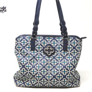 May include: A navy blue tote bag with a geometric pattern in teal and off-white. The bag has dark blue braided handles and a decorative silver-toned clasp. The text "KNOT SIMPLE Boutique" is in the upper left corner.