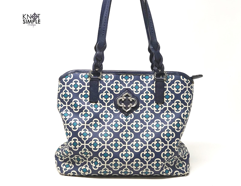 May include: A navy blue tote bag with a geometric pattern in teal and off-white. The bag has dark blue braided handles and a decorative silver-toned clasp. The text "KNOT SIMPLE Boutique" is in the upper left corner.