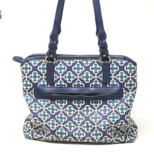 May include: A navy blue tote bag with a geometric teal and white pattern. The bag has navy blue handles and trim, a zippered top, and a front pocket. The bag has the text "KNOT SIMPLE" on the upper left corner.