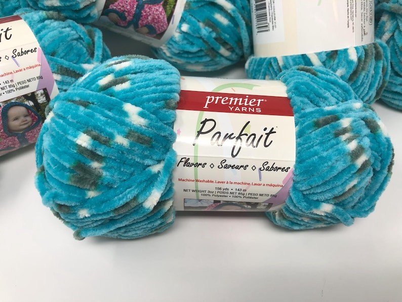 May include: A skein of Premier Yarns Parfait yarn featuring a soft, velvet-like texture in a variegated pattern of bright turquoise, white, and dark gray. The white paper label displays the brand name, product name, and a net weight of 3 oz.