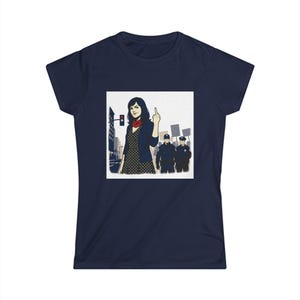 May include: Navy blue t-shirt featuring a pop art style image of a woman giving the middle finger in front of a city scene with police officers. The woman is wearing a black jacket, a red scarf, and a polka dot dress.
