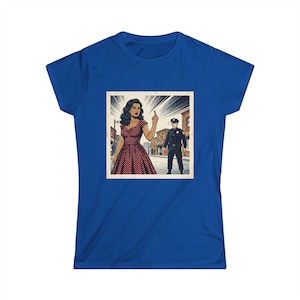 May include: A royal blue t-shirt featuring a square graphic print of a comic book style illustration. The image depicts a person in a red polka dot dress gesturing with a middle finger toward a police officer standing on a city street.
