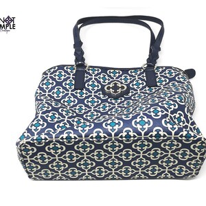 May include: Navy blue tote bag with a geometric pattern in teal and off-white. The bag has dark blue handles and trim, and a decorative clasp. The bag is from the Knot Simple Boutique.