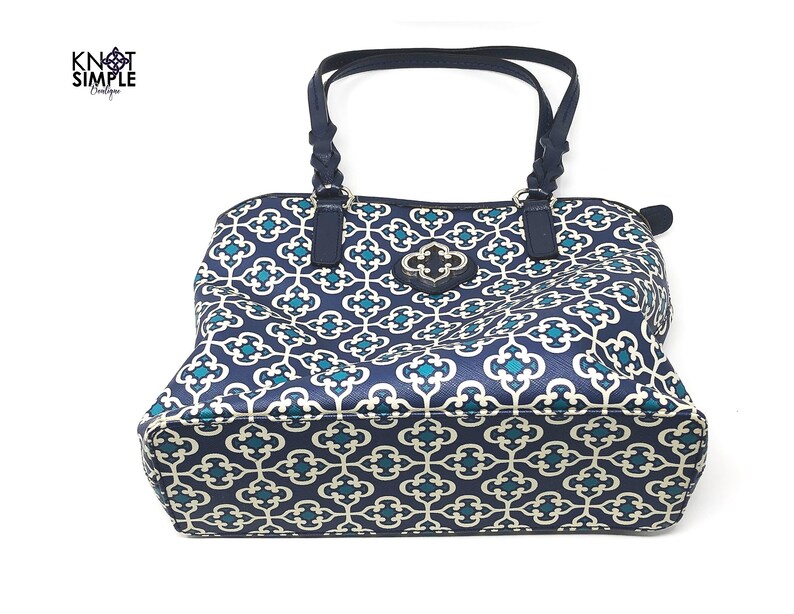 May include: Navy blue tote bag with a geometric pattern in teal and off-white. The bag has dark blue handles and trim, and a decorative clasp. The bag is from the Knot Simple Boutique.
