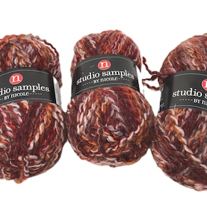 May include: Three balls of Studio Samples by Nicole yarn. The yarn is a mix of red, orange, and white fibers. Each ball has a black label with white text and a red "n" logo.