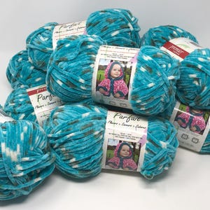 May include: A collection of Premier Yarns Parfait yarn skeins in a variegated teal, white, and dark gray colorway. Each skein features a soft, chenille-style texture and a paper label displaying a photograph of a child wearing a hooded garment.