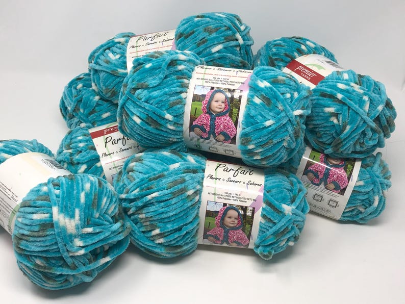 May include: A collection of Premier Yarns Parfait yarn skeins in a variegated teal, white, and dark gray colorway. Each skein features a soft, chenille-style texture and a paper label displaying a photograph of a child wearing a hooded garment.