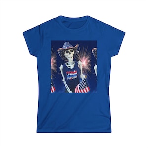 May include: A royal blue short-sleeve t-shirt featuring a central graphic of a skeleton wearing a cowboy hat patterned with stars and stripes. The skeleton wears a dark blue tank top with the word FREEDOM printed repeatedly and holds an American flag.