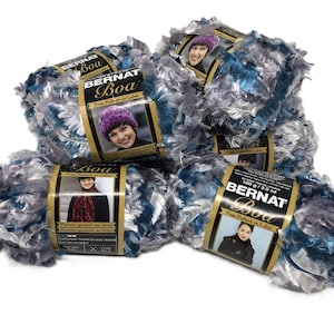 May include: Four skeins of Bernat Boa yarn in a variegated blue, silver, and black colorway. Each skein features a black paper label with the brand name, a photograph of a person wearing a garment made from the yarn, and a net weight of 3.5 oz.