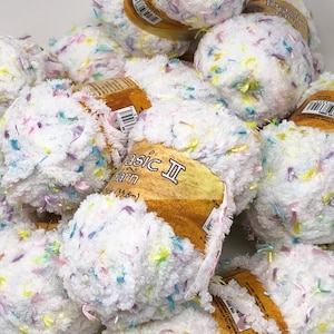 May include: A pile of white yarn balls with colorful flecks of blue, yellow, and pink. The yarn is labeled "Basic II Yarn". The texture appears soft and fluffy, ideal for knitting or crocheting projects.
