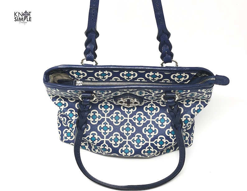 May include: A navy blue tote bag with a white and teal geometric pattern. The bag has braided navy blue handles and a silver clasp. The interior lining features a similar pattern. The bag is open, revealing the interior.