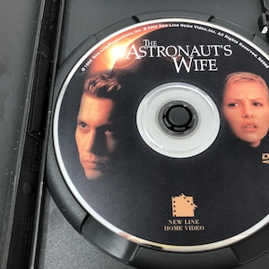 May include: DVD of the movie "The Astronaut's Wife" in a black case. The disc features images of the actors and the movie title. The DVD is labeled with the New Line Home Video logo.