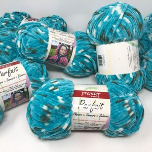 May include: A collection of Premier Yarns Parfait yarn skeins in a variegated turquoise, white, and dark gray colorway. Each skein features a white paper label with the brand name, product name, and a photograph of a child wearing a hooded garment.