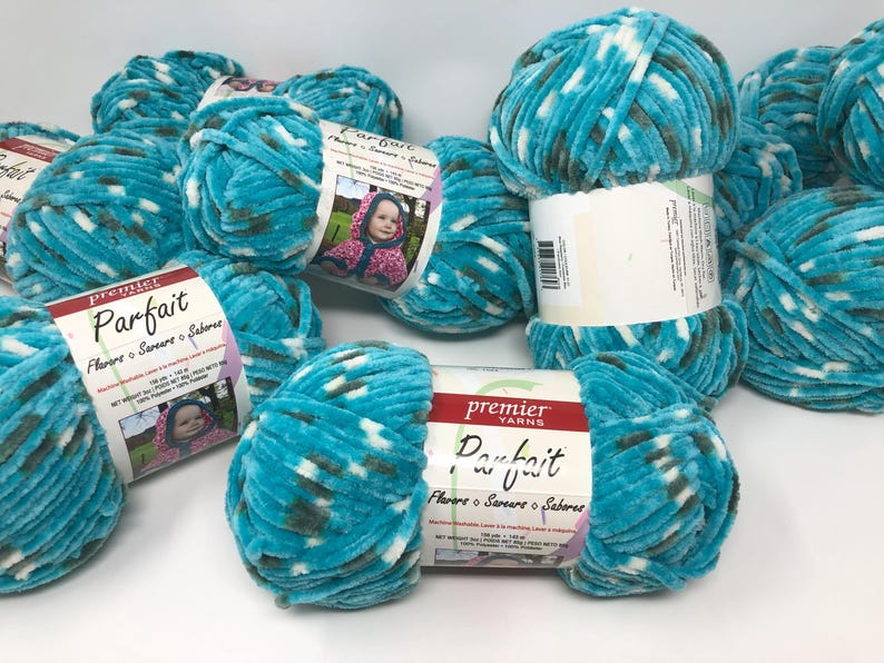 May include: A collection of Premier Yarns Parfait yarn skeins in a variegated turquoise, white, and dark gray colorway. Each skein features a white paper label with the brand name, product name, and a photograph of a child wearing a hooded garment.