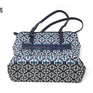 May include: Navy blue tote bag with a geometric pattern in teal and white. The bag features a zippered pocket and braided handles. The brand name "Knot Simple" is visible in the upper left corner.