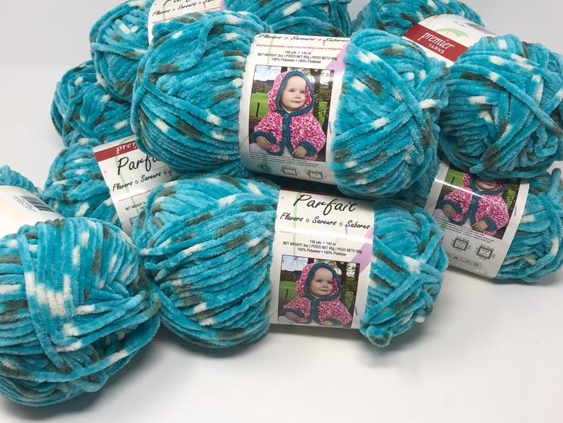 May include: A collection of Premier Yarns Parfait yarn skeins in a variegated turquoise, white, and dark gray colorway. Each skein features a paper label with the brand name, product name, and a photograph of a hooded garment in pink.