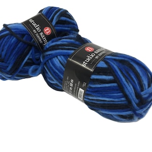 May include: Two skeins of thick, plush yarn featuring a variegated color palette of navy blue, royal blue, and light blue. Each skein is wrapped in a black paper band with the white text studio sample by nicole and a red circular logo.