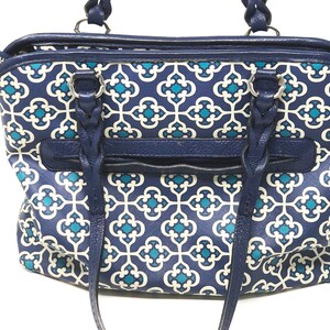 May include: A navy blue handbag with a geometric teal and white pattern. The bag features braided handles, a zippered top, and a front pocket. The bag's trim and handles are a solid navy blue.