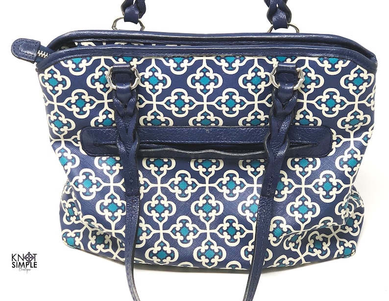 May include: A navy blue handbag with a geometric teal and white pattern. The bag features braided handles, a zippered top, and a front pocket. The bag's trim and handles are a solid navy blue.