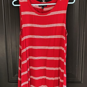 May include: Red tank top with horizontal white stripes. The sleeveless top is hanging on a light blue hanger. The top has a scoop neck and a slightly flared bottom hem.