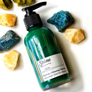 Puede incluir: Una botella de vidrio verde con un dispensador de bomba que contiene un l&iacute;quido verde. La botella tiene una etiqueta blanca con el texto "Shine Skincare Co." y "Greens + Ginseng Cleanser Chlorophyll, Green Tea, Spirulina".