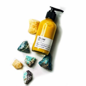 Puede incluir: Una botella de vidrio transparente de Shine Skincare Co. Nourish Body Serum con un dispensador de bomba negro. El suero amarillo est&aacute; rodeado de piedras preciosas de colores y en bruto sobre un fondo blanco.