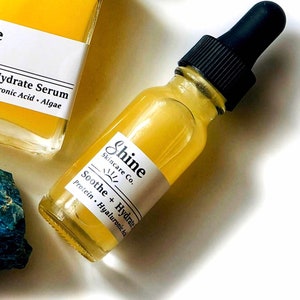 May include: A yellow glass bottle with a black dropper top. The bottle is labeled "Shine Skincare Co." and "Soothe + Hydrate Protein. Hyaluronic Acid."