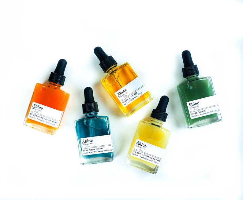May include: Five glass bottles with dropper tops containing different serums. The bottles are labeled with the brand name "Shine Skincare Co." and the names of the serums: "Brightening AHA Serum", "Super C + E Oil", "Blue Algae Serum", "Soothe + Hydrate Serum", and "Youth Serum".