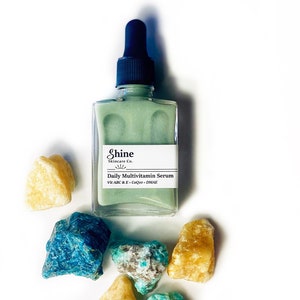 Op de afbeelding: Een groene glazen fles met een druppelaar, met het label "Shine Skincare Co. Daily Multivitamin Serum Vit A B C & E - CoQ10 - DMAE"