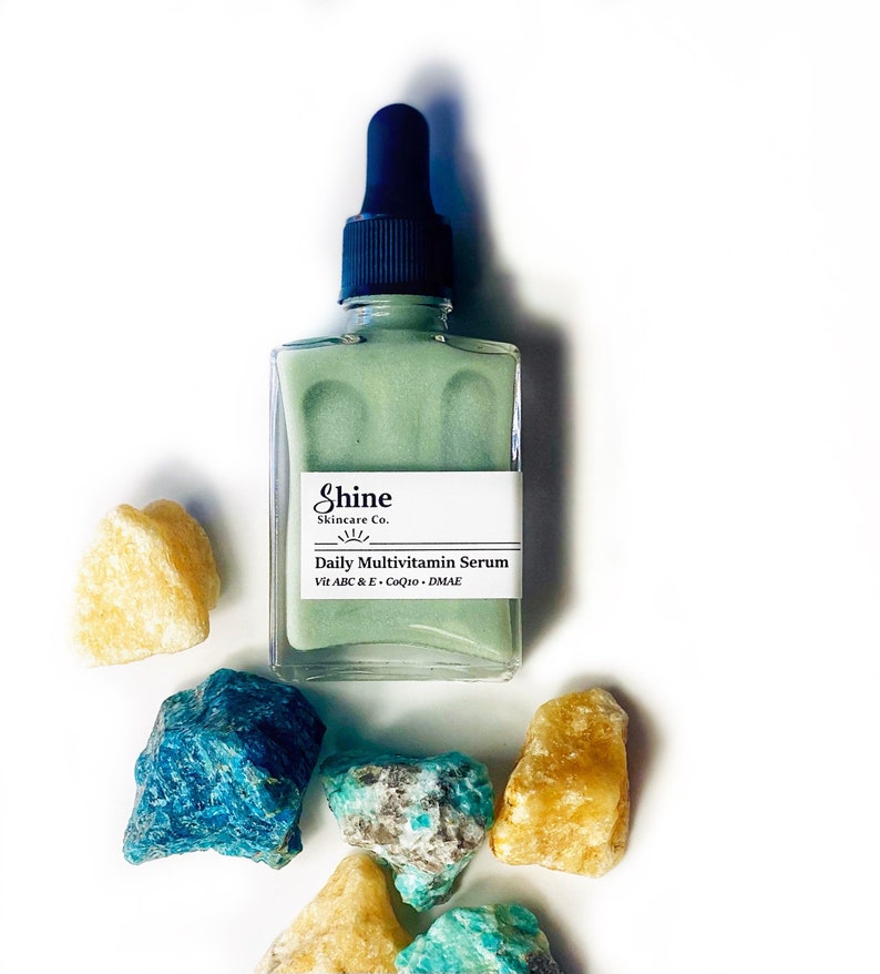 Op de afbeelding: Een groene glazen fles met een druppelaar, met het label "Shine Skincare Co. Daily Multivitamin Serum Vit A B C & E - CoQ10 - DMAE"