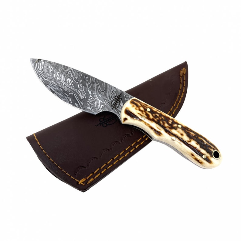 May include: A Damascus steel hunting knife with a stag horn handle and a brown leather sheath.