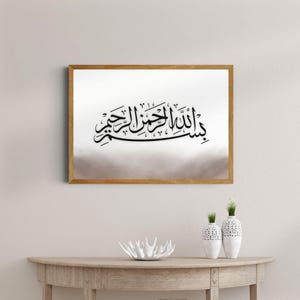 Op de afbeelding: Een ingelijste print met zwarte Arabische kalligrafie op een vage wit-bruine achtergrond. De houten lijst verbetert het kunstwerk, ideaal voor interieurdecoratie. Geschikt voor elke kamer.