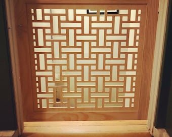 May include: A light-colored wooden baby gate with a geometric woven pattern. The gate is installed in a doorway with hardwood flooring. The gate's design features a series of rectangular cutouts, creating a decorative and functional barrier.