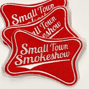 May include: Three red embroidered patches with white text and a white border. The patches read "Small Town Smokeshow" in a stylized font. The patches are stacked slightly, showing the design.