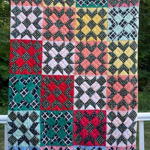 May include: A rectangular quilt featuring a repeating star block pattern. The quilt is composed of various fabric squares in shades of pink, yellow, green, red, light blue, and white, with dark patterned fabric accents forming the star shapes.
