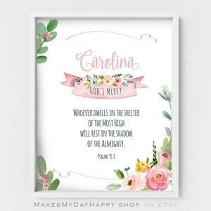 May include: A pink and white floral print with the name "Carolina" and the text "God's Mercy" in a pink banner. The text "Whoever dwells in the shelter of the Most High will rest in the shadow of the Almighty. Psalms 91:1" is printed below the banner.