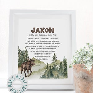 May include: A framed print with the name "JAXON" in brown letters. The print includes a watercolor illustration of a moose in a forest scene, with text describing the name's characteristics. A small plant in a terracotta pot is in the foreground.