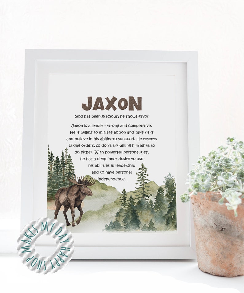 May include: A framed print with the name "JAXON" in brown letters. The print includes a watercolor illustration of a moose in a forest scene, with text describing the name's characteristics. A small plant in a terracotta pot is in the foreground.