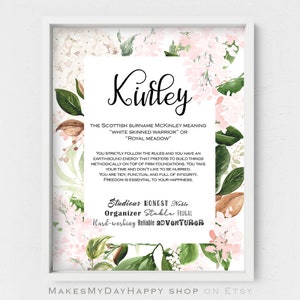 May include: A framed print featuring the name "Kinley" in elegant script. The print includes the meaning of the name, a description of the name's characteristics, and a floral and botanical design in shades of pink, green, and brown.