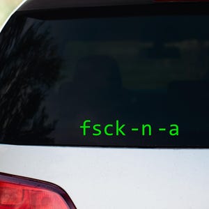 May include: A rear window of a silver car with a green sticker that says "fsck -n -a".