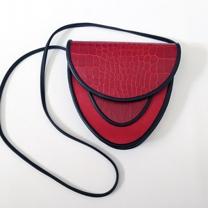 May include: A red leather crossbody bag with a black strap and a crocodile-embossed flap.