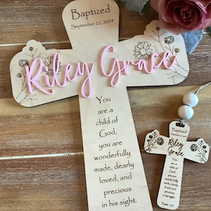 May include: A light-coloured wooden cross featuring the engraved text "Baptized September 22, 2024" and "You are a child of God, you are wonderfully made, dearly loved, and precious in his sight." The name "Riley Grace" is in raised pink script.