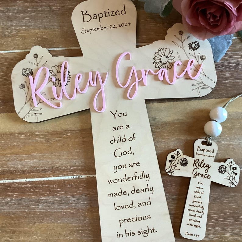 May include: A light-coloured wooden cross featuring the engraved text "Baptized September 22, 2024" and "You are a child of God, you are wonderfully made, dearly loved, and precious in his sight." The name "Riley Grace" is in raised pink script.