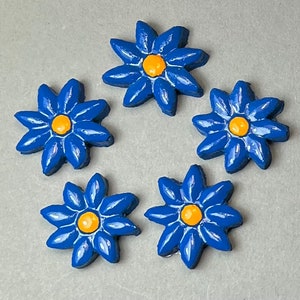 Könnte beinhalten: Fünf blaue Keramik-Blumenverzierungen mit gelben Zentren. Jede Blume hat sechs Blütenblätter.