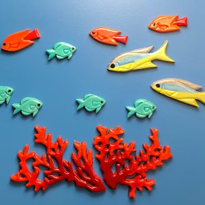 Könnte beinhalten: Eine Korallenriffszene mit roter Koralle, blauen und gelben Fischen sowie orangefarbenen Fischen. Die Fische sind aus Holz gefertigt und in leuchtenden Farben bemalt.