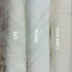 May include: Three rolls of tulle fabric in shades of white. The rolls are labelled "Off", "White", and "Light ivory". The fabric is tightly rolled, showing its texture and colour variations. Suitable for crafting and bridal projects.