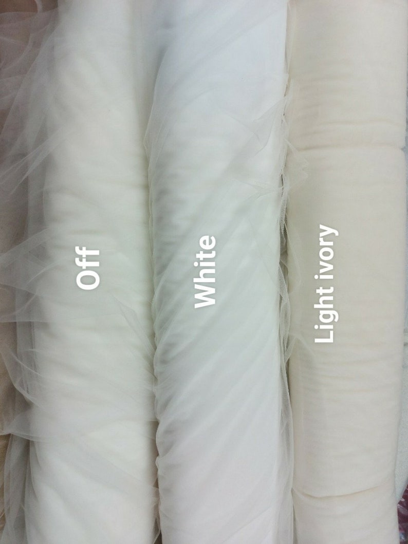 May include: Three rolls of tulle fabric in shades of white. The rolls are labelled "Off", "White", and "Light ivory". The fabric is tightly rolled, showing its texture and colour variations. Suitable for crafting and bridal projects.