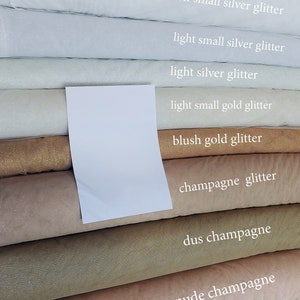 K&ouml;nnte beinhalten: Ein Stapel Tulle-Stoffrollen in verschiedenen Wei&szlig;-, Champagner- und Goldt&ouml;nen mit Glitzer. Die Stoffrollen sind mit den Farbnamen beschriftet: Wei&szlig;, leichtes, kleines Silberglitzer, leichtes, kleines Silberglitzer, leichtes Silberglitzer, leichtes, kleines Goldglitzer, Blush-Goldglitzer, Champagnerglitzer, staubiger Champagner, Nude-Champagner und elfenbeinfarbenes Goldglitzer.